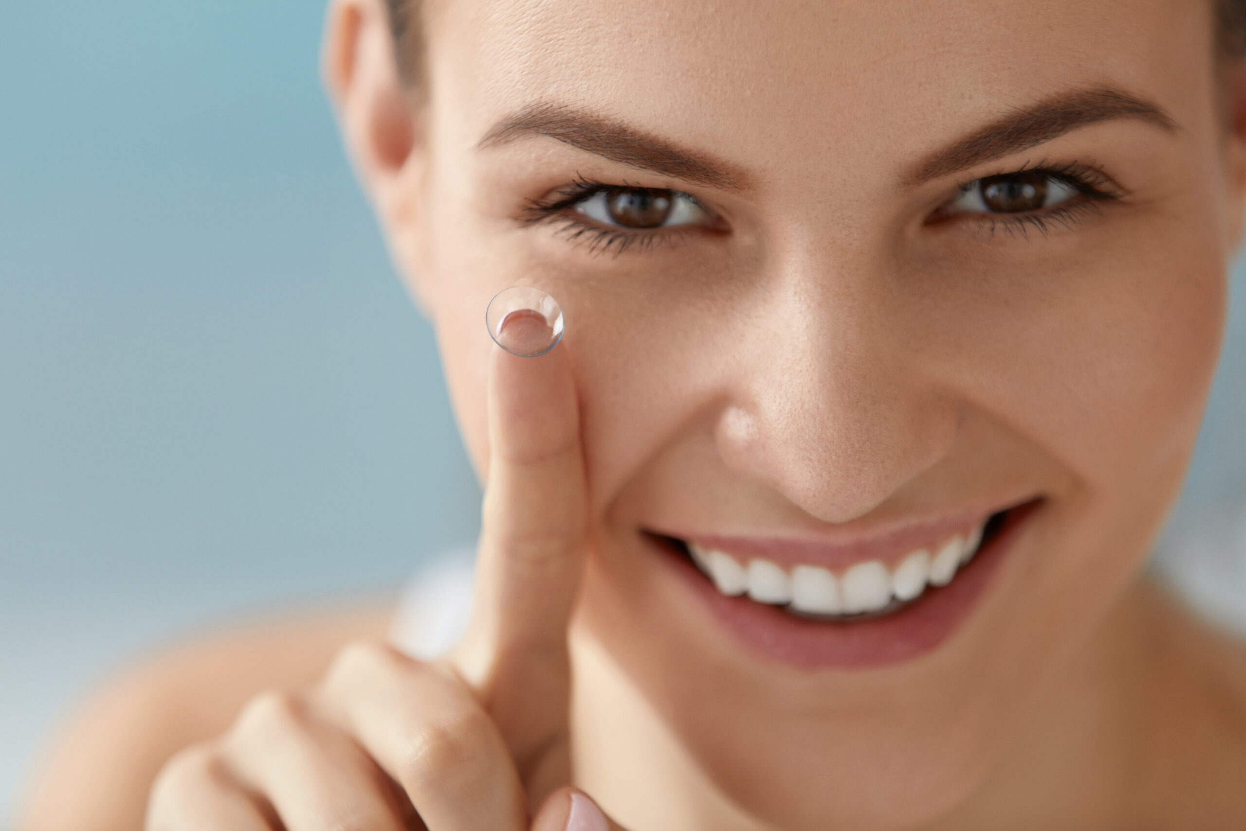 Eye care. Smiling woman with contact eye lens on finger closeup
