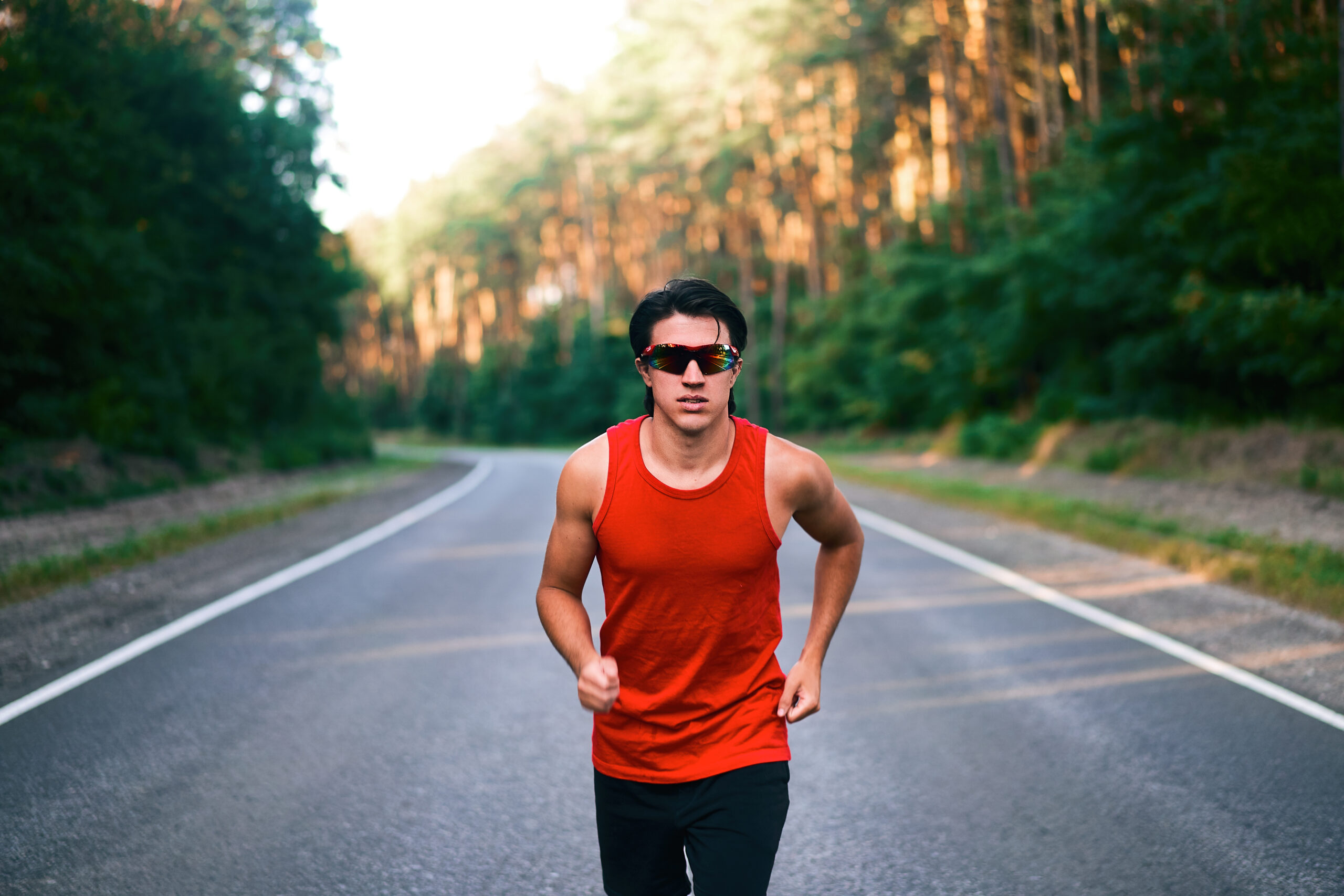Caucasian middle age man athlete runs sunny summer day on asphalt road in the forest.